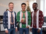Three coworkers laughing at an office Christmas party in muscle Christmas sweaters in navy snowflake, green snowflake and red Fair Isle, each with the skin tone that matches his own Three coworkers laughing at an office Christmas party in muscle Christmas sweaters in navy snowflake, green snowflake and red Fair Isle, each with the skin tone that matches his own